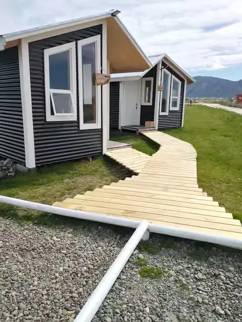 Pasarela de madera hacia la entrada de Cabaña Encanto con cartel tallado en madera y montañas al fondo
